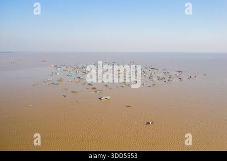 Bunte schwimmende Häuser und Boote verstreut über das weitläufige braune Wasser des Tonle SAP Sees in Chong Kneas, Kambodscha. Der weite Blick aus der Luft zeigt die einzigartige Wassergemeinschaft unter einem klaren blauen Himmel. Stockfoto