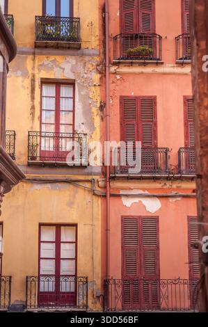 Verwitterte rosa und gelbe Altstadtgebäudefassade mit grünen Fensterläden und schmiedeeisernen Balkonen, mediterrane Architektur Stockfoto
