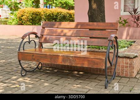 Eine einzigartige Holzbank mit Rückenlehne unter dem Baum im Vorhof des Hauses Stockfoto
