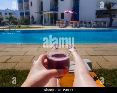 Eine Frau hält ein Glas Wein, während sie mit den Füßen auf einer Liege sitzt Stockfoto