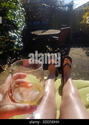 Eine Frau hält ein Glas Wein, während sie mit den Füßen auf einer Liege sitzt Stockfoto