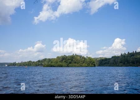 Eine üppig grüne Insel erhebt sich aus dem sanften Wasser des Lac des Settons, umgeben von einem plätschernden blauen See und unter einem Himmel voller geschwollener weißer Wolken. Stockfoto