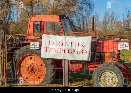 Traktor hinter einem Zaun mit einem Banner mit der Aufschrift „Shuttles to the Church“ – ländliche Ausrüstung in Nord-Buda-Feuchtgebieten in Budapest. Stockfoto