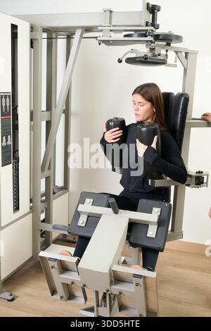Junge Frau, die ein Kerntraining auf spezialisierten Fitnessgeräten durchführt. Konzentration auf Fitnessentwicklung und Krafttraining Stockfoto
