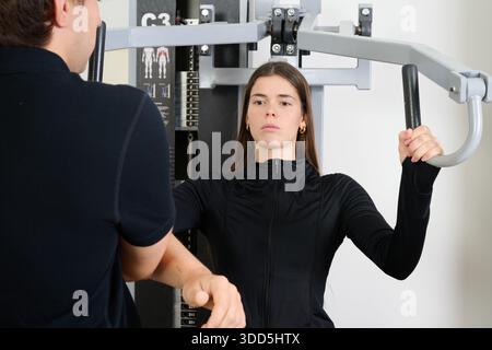 Frau, die ein Brusttraining mit Unterstützung eines männlichen Personal Trainers in einem Fitnessstudio durchführt. Konzentrieren Sie sich auf Fitness und Beratung Stockfoto