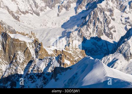 Weite Sicht auf dramatische schneebedeckte Hänge und zerklüftete Granitgipfel im Mont Blanc-Massiv, mit tiefblauen Schatten und klarem Winterlicht, das die alpinen Strukturen unterstreicht. Stockfoto