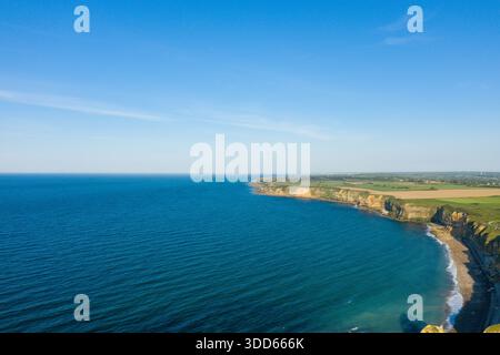 Weite Aussicht aus der Vogelperspektive auf die weitläufige Küste von Pointe du hoc, Normandie, mit tiefblauem Meer, schroffen Klippen und fleckigen Ackerflächen unter klarem Himmel. Stockfoto