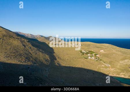 Kleine Ansammlung ländlicher Häuser auf goldenen Hügeln mit Blick auf das tiefblaue Mittelmeer in Cap Tenare, Griechenland. Die weite, offene Landschaft wird von klarem Sonnenlicht unter einem weiten Himmel beleuchtet, was Einsamkeit und natürliche Schönheit hervorruft. Stockfoto