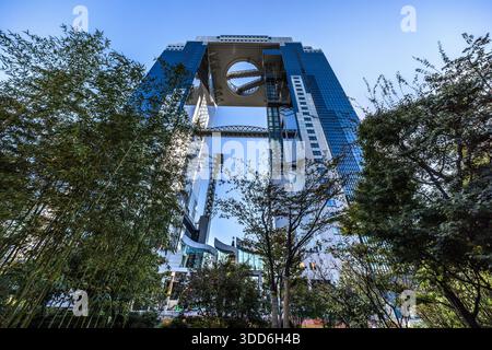 Das Umeda Sky Building erhebt sich hinter Bäumen und Bambus in Osaka, Japan. Die Zwillingsürme des 173 Meter hohen Gebäudes, das 1993 vom Architekten Hiroshi Hara fertiggestellt wurde, sind im 39. Stock durch das ringförmige „Floating Garden Observatory“ verbunden. Stockfoto