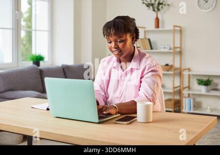 Junge afroamerikanische Frau, die an ihrem Schreibtisch sitzt und am Laptop arbeitet Stockfoto
