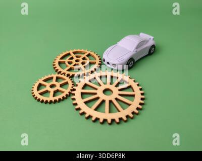 Kleines weißes Spielzeugauto und mehrere lasergeschnittene Holzzahnräder auf grünem Hintergrund. Stockfoto