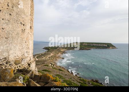 Der verwitterte Steinturm erhebt sich über der zerklüfteten Küste von Capo San Marco auf Sardinien und bietet einen Panoramablick auf die Halbinsel und das Mittelmeer unter einem weichen, bewölkten Himmel. Stockfoto