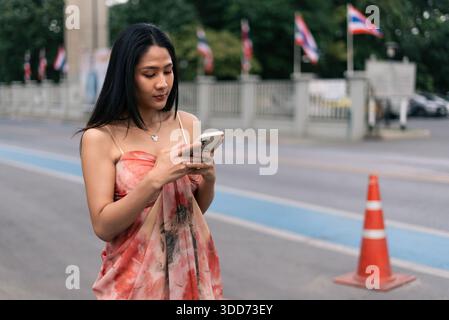 Junge Frau, die auf dem Smartphone mit thai-Fahnen und Verkehrskegel schreibt Stockfoto