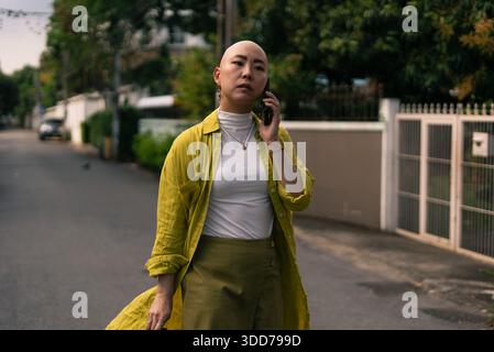 Kahle asiatische Frau, die beim Gehen telefoniert, spiegelt einen selbstbewussten Lebensstil wider Stockfoto
