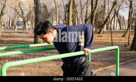 Entschlossener Mann, der draußen Einbrüche an parallelen Balken durchführt. Stockfoto