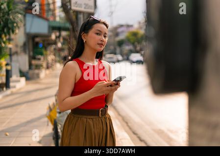 Asiatische Frau, die auf dem Smartphone in der Stadtstraße schreibt und sich mit Technologie beschäftigt Stockfoto