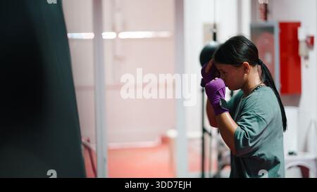 Entschlossene junge Frau, die Boxen im Fitnessstudio trainiert, sich auf das Fitnesstraining vorbereitet Stockfoto