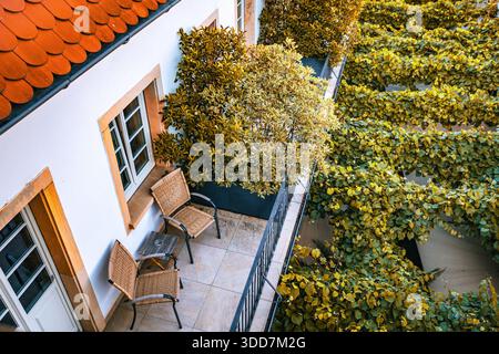 Blick von oben auf einen Balkon mit Tisch und zwei Stühlen, umgeben von üppigem Grün. Stockfoto