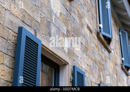Eine Nahaufnahme einer verwitterten Steinmauer mit dunkelblauen Fensterläden, die ein rustikales und charmantes architektonisches Detail zeigt. Stockfoto
