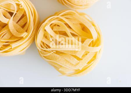 Eine detaillierte Makroaufnahme roher Tagliatelle-Pasta, wunderschön in goldenen Spulen angeordnet. Das Bild hebt die Textur und natürliche Farbe der Tradition hervor Stockfoto