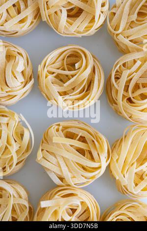 Eine detaillierte Makroaufnahme roher Tagliatelle-Pasta, wunderschön in goldenen Spulen angeordnet. Das Bild hebt die Textur und natürliche Farbe der Tradition hervor Stockfoto