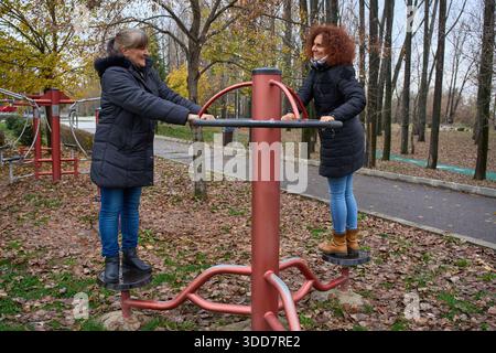 Zwei Freundinnen, die gemeinsam in einem Herbstpark Outdoor-Fitnessgeräte nutzen Stockfoto