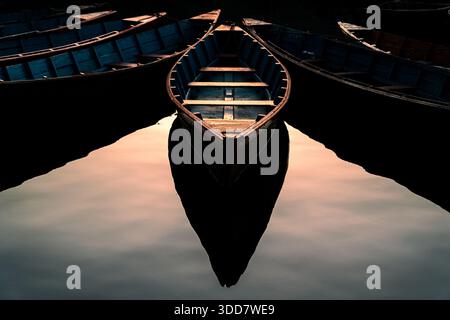 Eine symmetrische Komposition traditioneller hölzerner Ruderboote, die auf stillem Wasser schweben und eine spiegelähnliche Reflexion erzeugen. Stockfoto