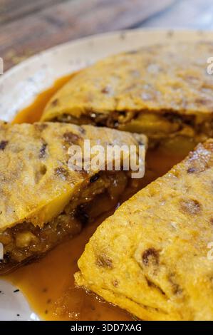Scheiben von traditionellem spanischem Kartoffelomelett (Tortilla de patata) in einer herzhaften Sauce gebadet Stockfoto