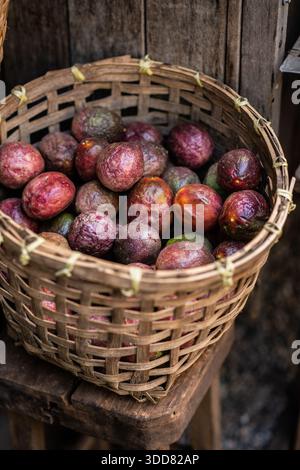 Reife Passionsfrüchte werden in einem gewebten Bambuskorb auf einem lokalen Markt präsentiert und zeigen tropische Landwirtschaft, Bio-Produkte und rustikale Texturen. Stockfoto