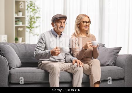 Glückliches, reifes Paar, das auf einem Sofa sitzt und Kaffee in einer Wohnung trinkt Stockfoto