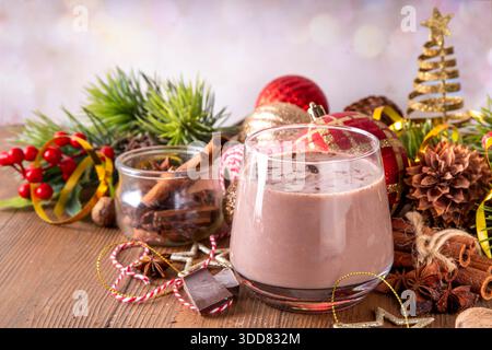 Gewürzter Schokoladen-Eierlikör-Punsch-Cocktail, serviert mit Zimtstab, Muskatnuss und Schokolade, auf gemütlichem Weihnachtshintergrund Stockfoto
