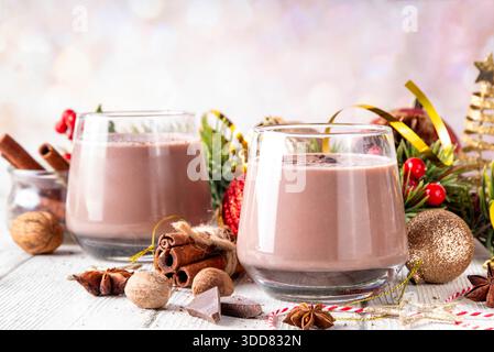 Gewürzter Schokoladen-Eierlikör-Punsch-Cocktail, serviert mit Zimtstab, Muskatnuss und Schokolade, auf gemütlichem Weihnachtshintergrund Stockfoto