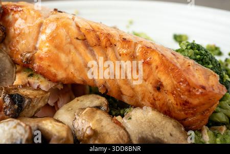 Ein Stück gegrillter Lachs wird neben Brokkoli und Pilzen auf einem weißen Teller platziert. Dieses Gericht wird in einem Restaurant während der Mittagsstunden mit Bright serviert Stockfoto