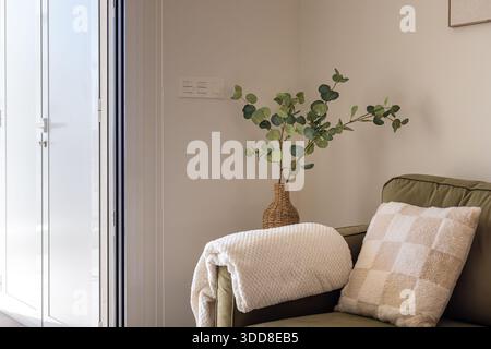 Sanft beleuchtete Ecke mit olivgrünem Sofa, Überwurfdecke, Kissen und Korbvase Stockfoto