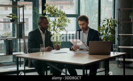 Zwei glückliche, vielfältige Geschäftsmänner, Team-Verträge unterzeichnen Dokumente Teamwork Zusammenarbeit multirassische Geschäftsleute Kaukasier und Afroamerikaner Stockfoto