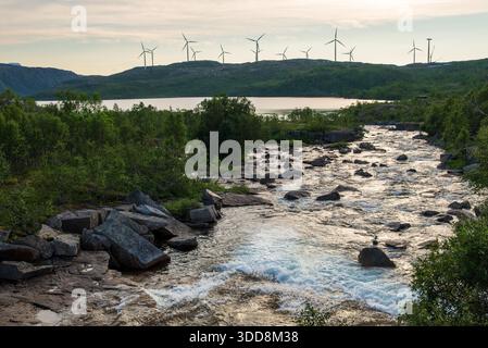 Ein kleiner Fluss mit fließendem Wasser in den norwegischen Bergen mit einem Windpark im Hintergrund. Stockfoto