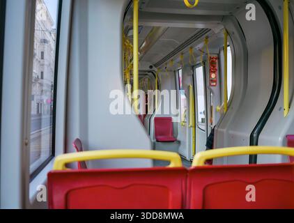 Moderner Straßenbahninnenraum mit leeren roten Sitzen und gelben Handläufen. Öffentliche Verkehrsmittel, Innenansicht, Stadtreisekonzept, Stadtpendelstrecke, sauberes Fahrzeug c Stockfoto
