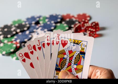 Spieler hält einen gewinnenden Straight Flush mit Casino Chips und Würfeln im Hintergrund Stockfoto
