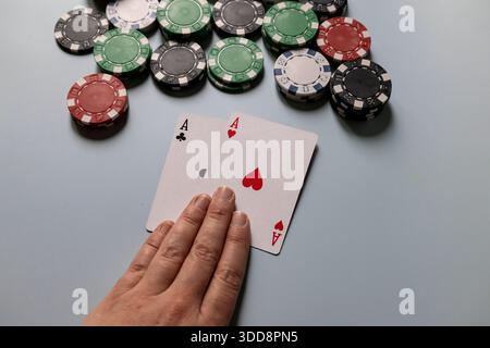 Spieler hält zwei Asse bei einem Pokerspiel mit Casino-Chips auf dem Tisch Stockfoto
