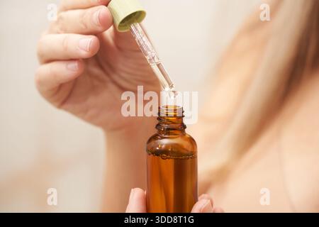 Weibliche Hand mit Tropfer Hautpflegeserum aus bernsteinfarbener Flasche für Schönheit und Selbstpflege. Stockfoto