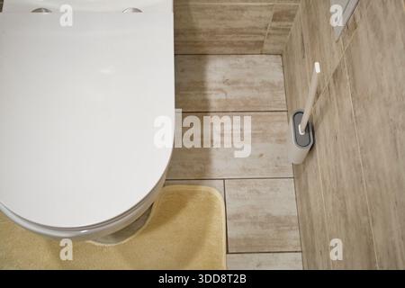 Moderne Toilettenschüssel mit geschlossenem Deckel und Reinigungsbürste im gefliesten Badezimmer Stockfoto