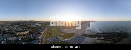 Blick aus der Vogelperspektive auf das goldene Sonnenlicht, das den weitläufigen West Sands Beach und den historischen Golfplatz küsst, im Kontrast zum Stadtbild St. Andrews, Scotla Stockfoto