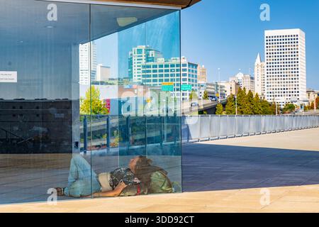 Tacoma, WA, USA - 20. September 2025: Eine Person, die Obdachlosigkeit erfährt, schlafend auf der Chihuly Bridge of Glass in Tacoma, gesehen gegen die Stadt SK Stockfoto