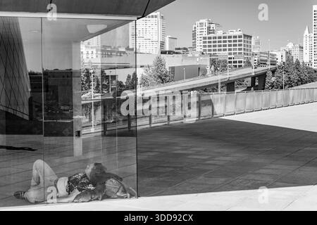Tacoma, WA, USA - 20. September 2025: Eine Person, die Obdachlosigkeit erfährt, schlafend auf der Chihuly Bridge of Glass in Tacoma, gesehen gegen die Stadt SK Stockfoto