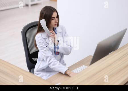 Ärztliche Assistentin, die am Computer am Empfang in der Klinik telefoniert Stockfoto