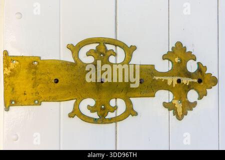 Verziertes Türscharnier aus Messing mit Vintage-Dekorationsbeschlägen an weißer Holztür Stockfoto