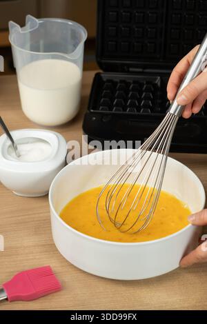 Mit einem Schneebesen die rohen Eier in einer weißen Schüssel zum Backen von Waffeln mischen Stockfoto