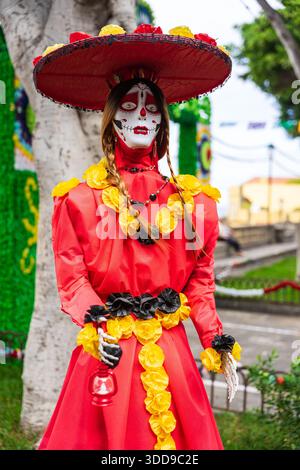 Festivalpuppe in rotem Kleid und breitem Hut mit bemaltem Schädelkopf und gelben Papierblumen während der Fiesta de la Muerte auf den Kanarischen Inseln. Stockfoto
