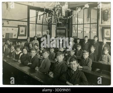 Originalfoto von Schulkindern aus den 1930er Jahren, die mit einem Lehrer in einem Klassenzimmer sitzen. Die Schülerinnen in der Klasse sind Mädchen und Jungen, die an Schreibtischreihen sitzen, Großbritannien Stockfoto