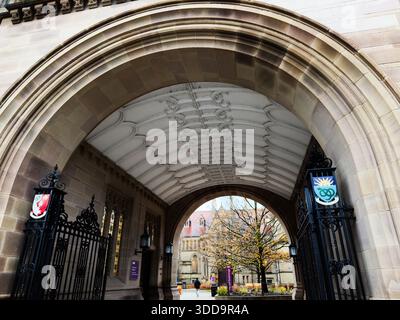 Manchester, Großbritannien - 06. Dezember 2025: Berühmter Torbogen der Universität Manchester mit Wappen, Sandsteintüren und einem mit Bäumen gefüllten Innenhof. Stockfoto